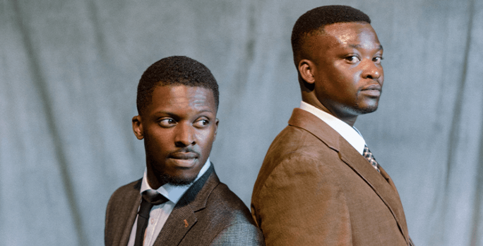 Two black men in suits look serious as they stand back to back