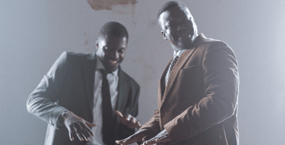 Two black men in suits smile as they dance together