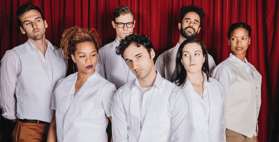 A group of people wearing white shirts stand in front of a red curtain
