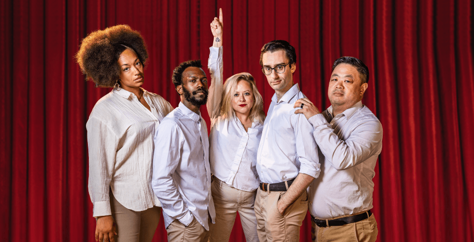 A group of people in white stand in formation in front of a red curtain