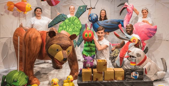 A group of people stand in white surrounded by large puppets of colourful characters from Eric Carle's stories