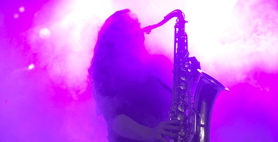 A saxophone player stands in a pink haze with a spotlight behind them