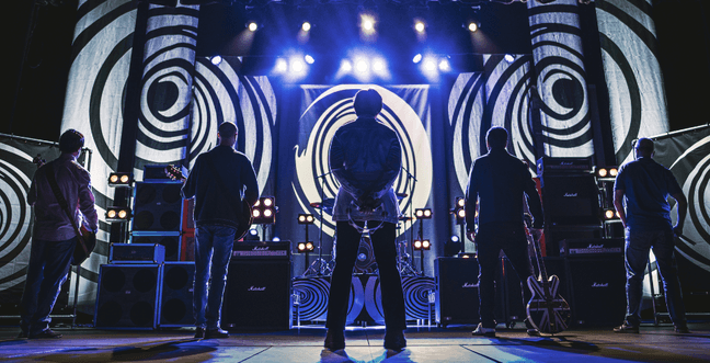 A silhouette of a band on stage backed by a projection of black and white psychedelic spirals