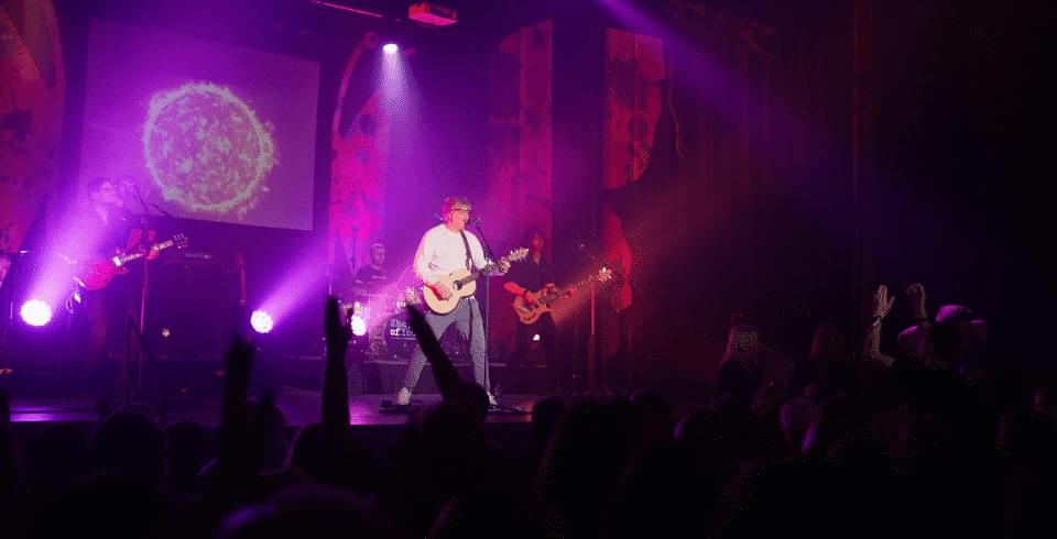 A man with a guitar in the pink spotlight on stage