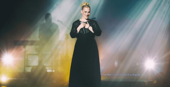A singer onstage in a black long dress with yellow and blue lights behind her.