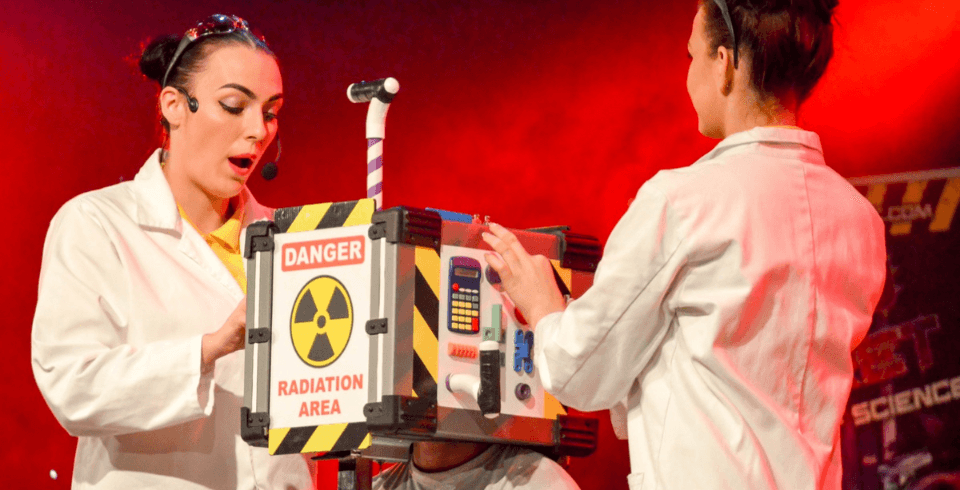 Two scientists in white lab coats on stage by a box that says 'danger'