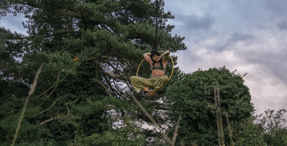 A woman hangs mid-air in trees on a hoop with her hand covering her face
