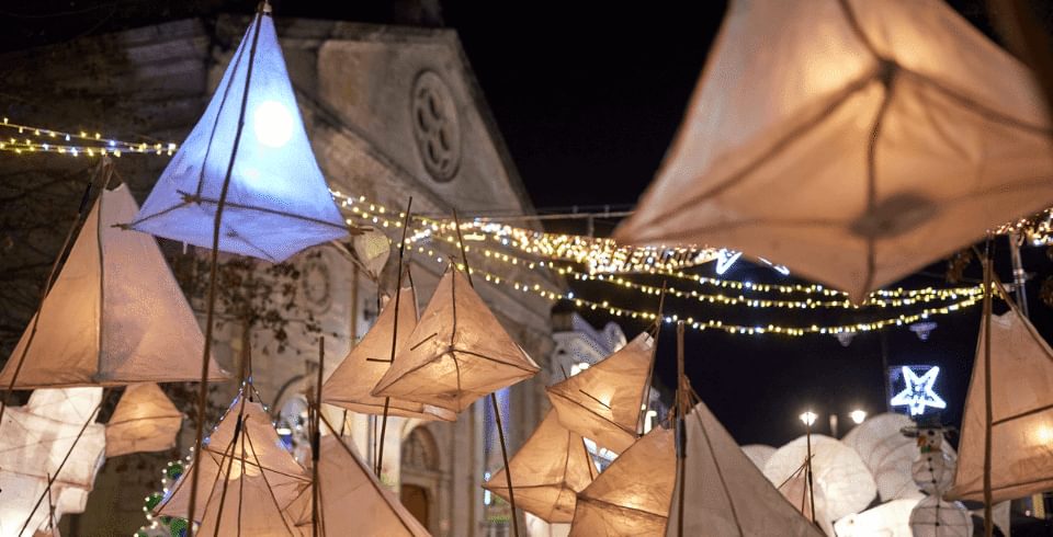 A collection of triangle lit-up lanterns in front of the Corn Exchange stone building at night