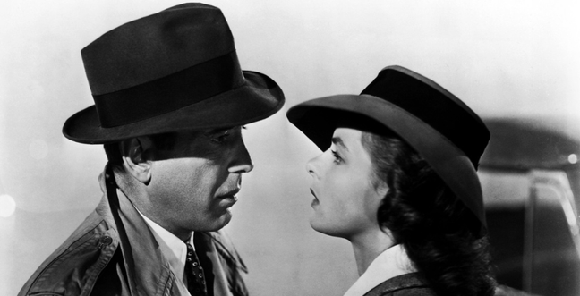 A couple in black and white wear dark top hats while they look into each others eyes