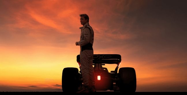 A racing drive stands behind his race car, silhouetted against the sunset