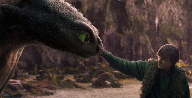 A boy cautiously reaching out to touch the nose of a dragon with black scales and green eyes.