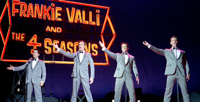 Four men in grey suits stand in front of a red neon sign that reads Frankie Valli and the 4 Seasons