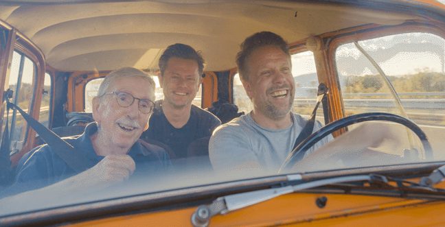 Three men smile in a yellow car