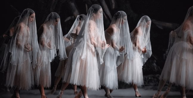 A group of female dancers all dressed in white and wearing sheer veils over their faces.