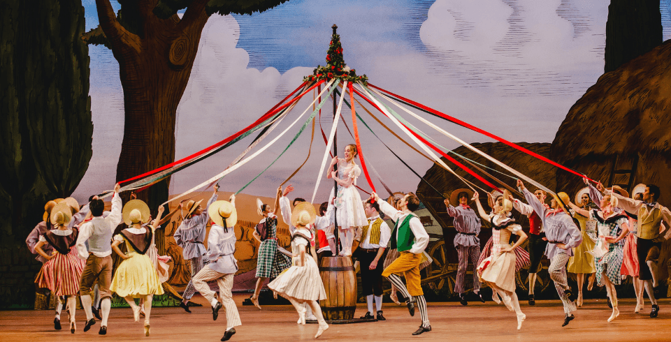 A large number of people dance around a colourful maypole