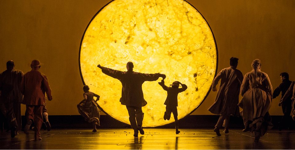 Adults and children run on stage lit by a large golden yellow moon