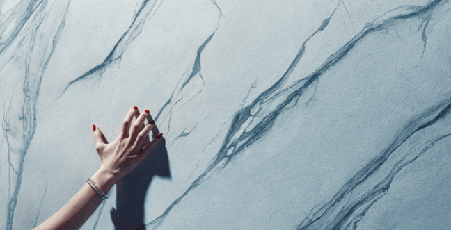 A woman's hand with red painted nails and a silver bracelet is pushed up against a marble wall
