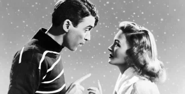 A man and woman in black and white look into each others eyes surrounded by snow with their hands almost touching