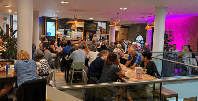 A group of people sat at wooden tables with warm lighting