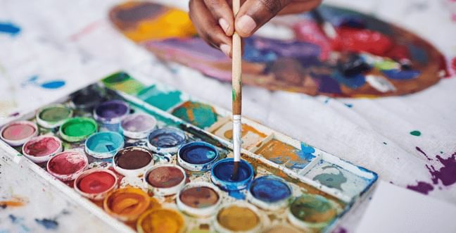 A watercolour pallet with a person getting paint using a paint brush.