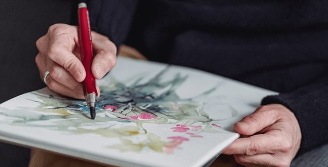 A person using a paint pen to draw on a pad of paper.