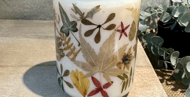 White wax candle in a large glass jar. Decorated with dried leaves and flowers.