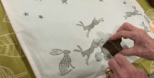 A woman's hands can be seen printing grey images of stars and rabbits onto a cream cushion cover