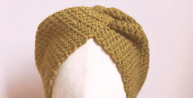 A greeny brown crochet twisted headband sits on top of a plain white mannequin head