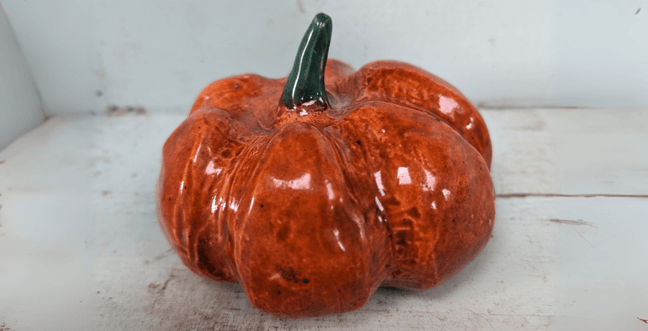 A glazed ceramic pumpkin in orange with a brown stalk