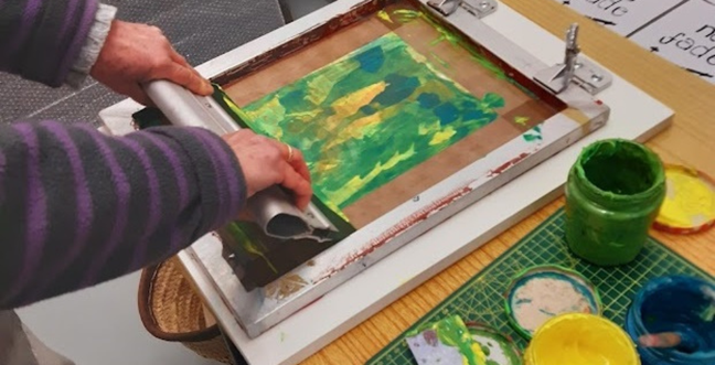 Two hand with a silk screen, printing in green and yellow ink