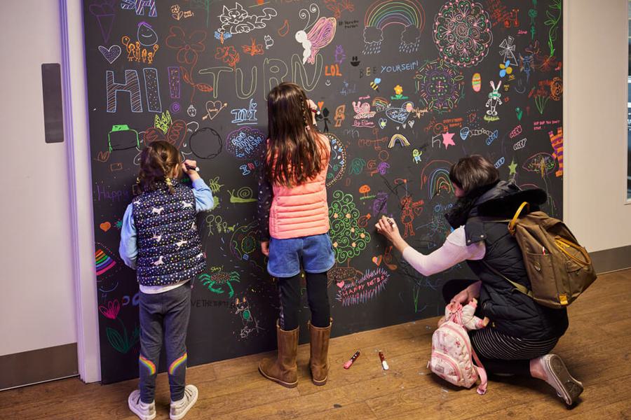 Children stand drawing on a chalkboard wall