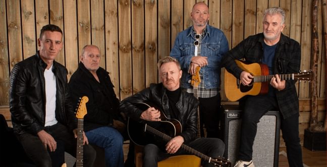 Five men dressing in leather jackets holding guitars and some sitting on guitar amps.