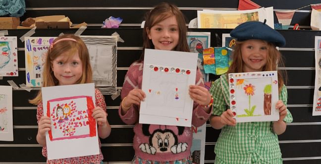 Three little girls proudly holding up their drawings.