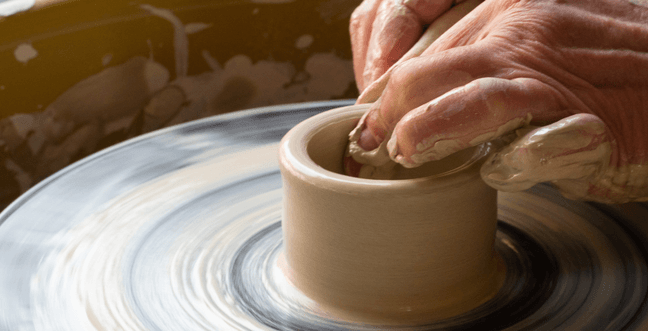 A pair of hands moulding clay on a pottery wheel