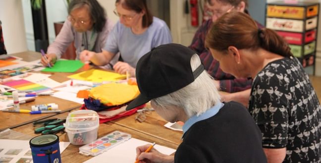 A group of women sit around a wooden table painting with watercolours